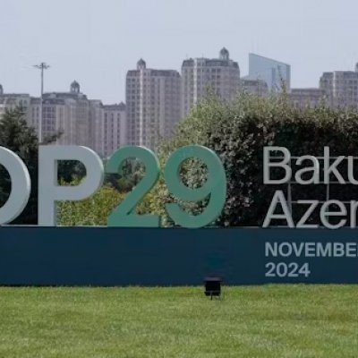 A large sign on a green lawn says COP20 Baku Azerbaijan with tall buildings in the background